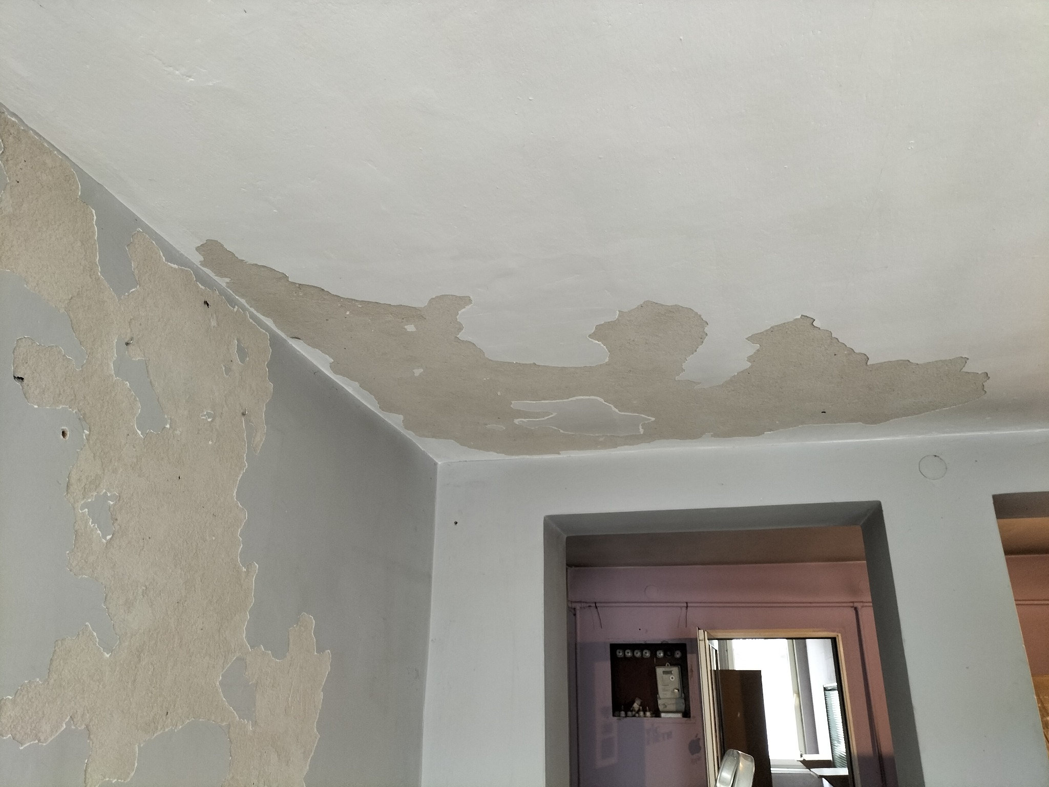 Zdjęcie przedstawia fragment pokoju z uszkodzonym sufitem i ścianami, gdzie widać odpadający tynk i warstwy wykończeniowe, ukazując stan przed remontem lub w trakcie jego wykonywania.