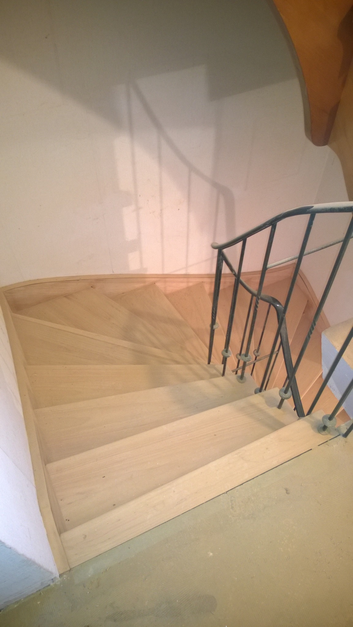 Jasne, drewniane schody z czarną, metalową balustradą widziane z góry, podczas remontu, z widocznymi śladami pyłu na podłodze.