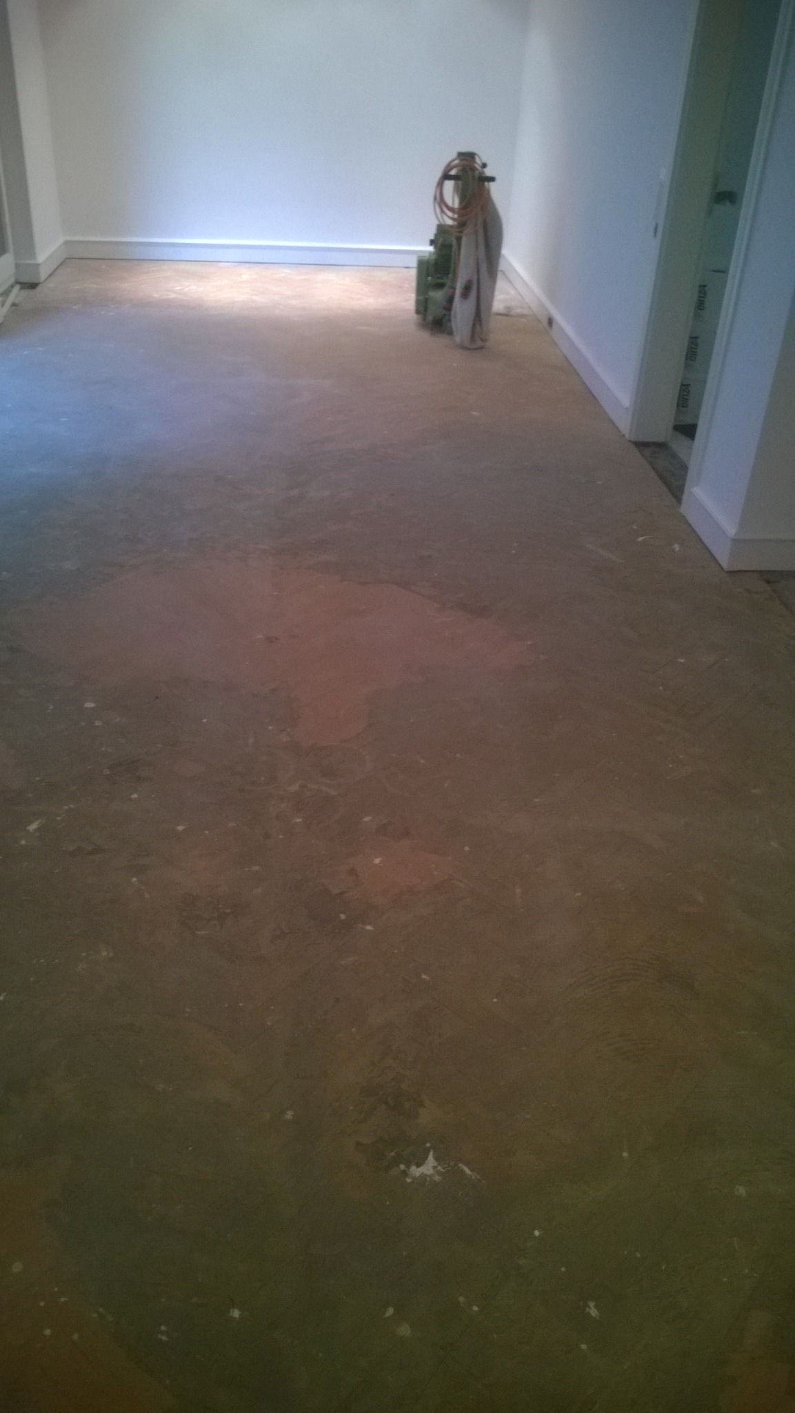 Szlifowany parkiet w trakcie renowacji, widoczna maszyna do cyklinowania przy ścianie, przygotowanie do lakierowania.