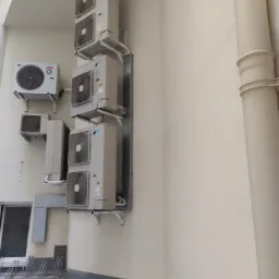 Zewnętrzne jednostki klimatyzacyjne Daikin zamontowane na ścianie budynku, widoczne rury i wsporniki montażowe, na dole stojak na rowery.