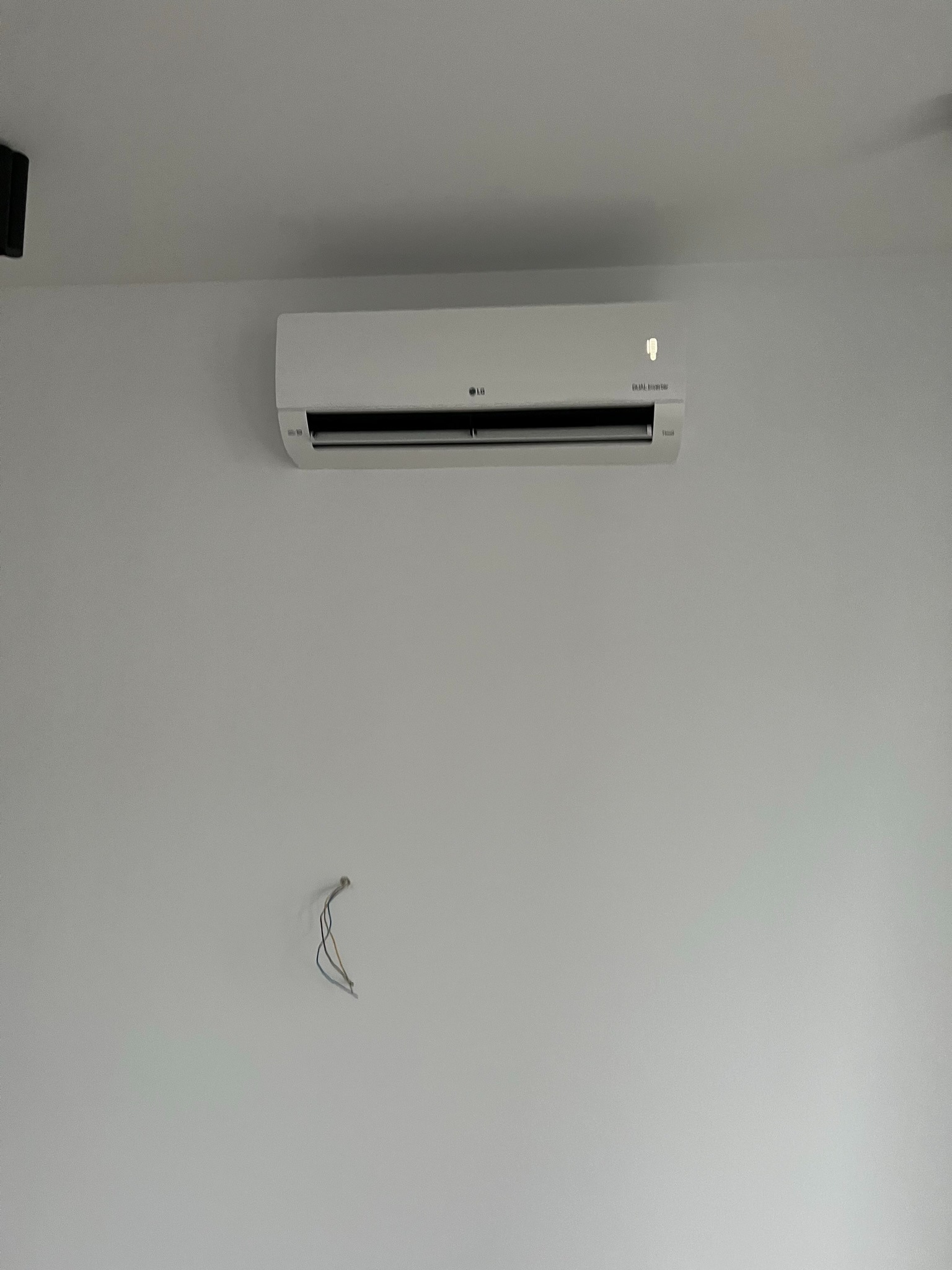 Biały klimatyzator LG Dual Inverter zamontowany na białej ścianie, widoczne wystające przewody elektryczne poniżej.