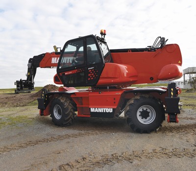 Czerwona ładowarka teleskopowa Manitou MRT 2145 Easy na żwirowym terenie, z wysuniętym ramieniem i osprzętem roboczym w pobliżu niewielkiego kopca ziemi.