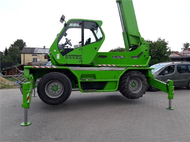 Zielona ładowarka teleskopowa Merlo 45.21 z wysuniętymi podporami, zaparkowana na kostce brukowej, widok z boku.