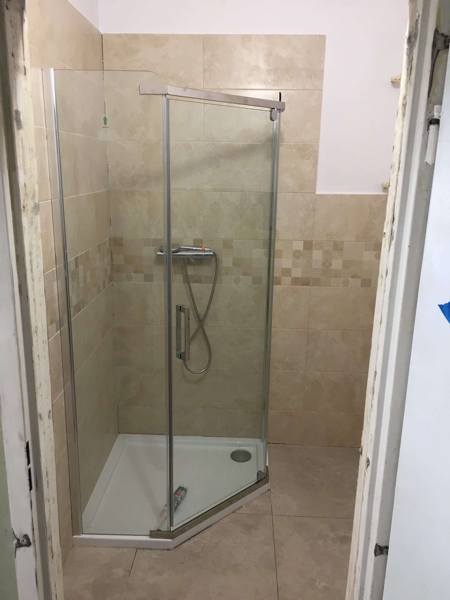 Kabina prysznicowa z chromowaną armaturą i beżowymi płytkami ceramicznymi w łazience podczas prac wykończeniowych, widoczna silikonowa tuba w brodziku.