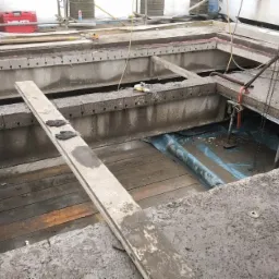 Prace przygotowawcze do remontu stropu w Piotrkowie Trybunalskim: otwory w betonowej konstrukcji, widoczne drewniane elementy i narzędzia, zabezpieczenie folią budowlaną.