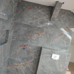 Ściana łazienki wyłożona szarymi płytkami imitującymi marmur z pomarańczowymi żyłami, widoczne niebieskie taśmy maskujące na krawędziach, przygotowane otwory na armaturę i fragment dokumentacji...