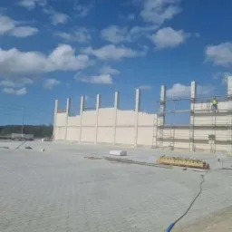 Budowa hali w strefie ekonomicznej: wznoszenie ścian z prefabrykat&oacute;w betonowych, widoczne rusztowania i pracownicy na wysokości.