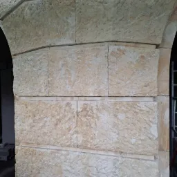 Fragment łuku z piaskowca, z widocznymi śladami obróbki kamieniarskiej i drobnymi uszkodzeniami powierzchni, z fragmentem rynny spustowej w górnej części.