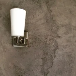 Ścienny kinkiet z białym kloszem i chromowaną podstawą, zamontowany na szarej ścianie z efektem betonu architektonicznego.