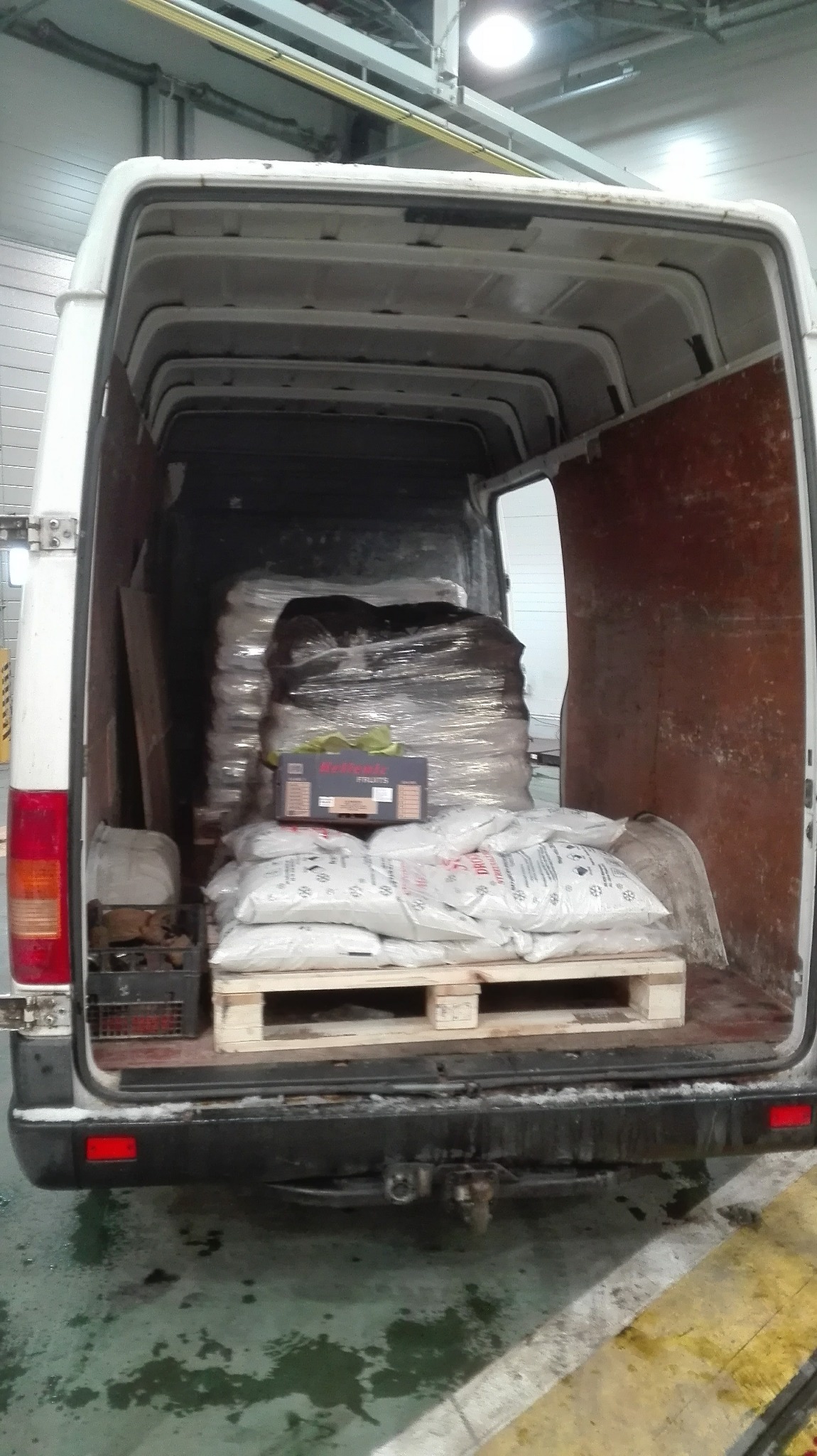 Wnętrze busa załadowane workami na palecie, kartonem owoców i towarem owiniętym folią stretch, widoczne ślady użytkowania na podłodze i zderzaku.