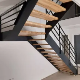 Nowoczesne schody z drewnianymi stopniami i czarną metalową konstrukcją, minimalistyczny design, widok z dołu, jasne wnętrze.