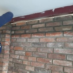 B4 & AFTER - Murarz poprawia wykończenie ściany z czerwonej cegły, widoczna poziomica i stalowa belka pod sufitem z resztkami farby.