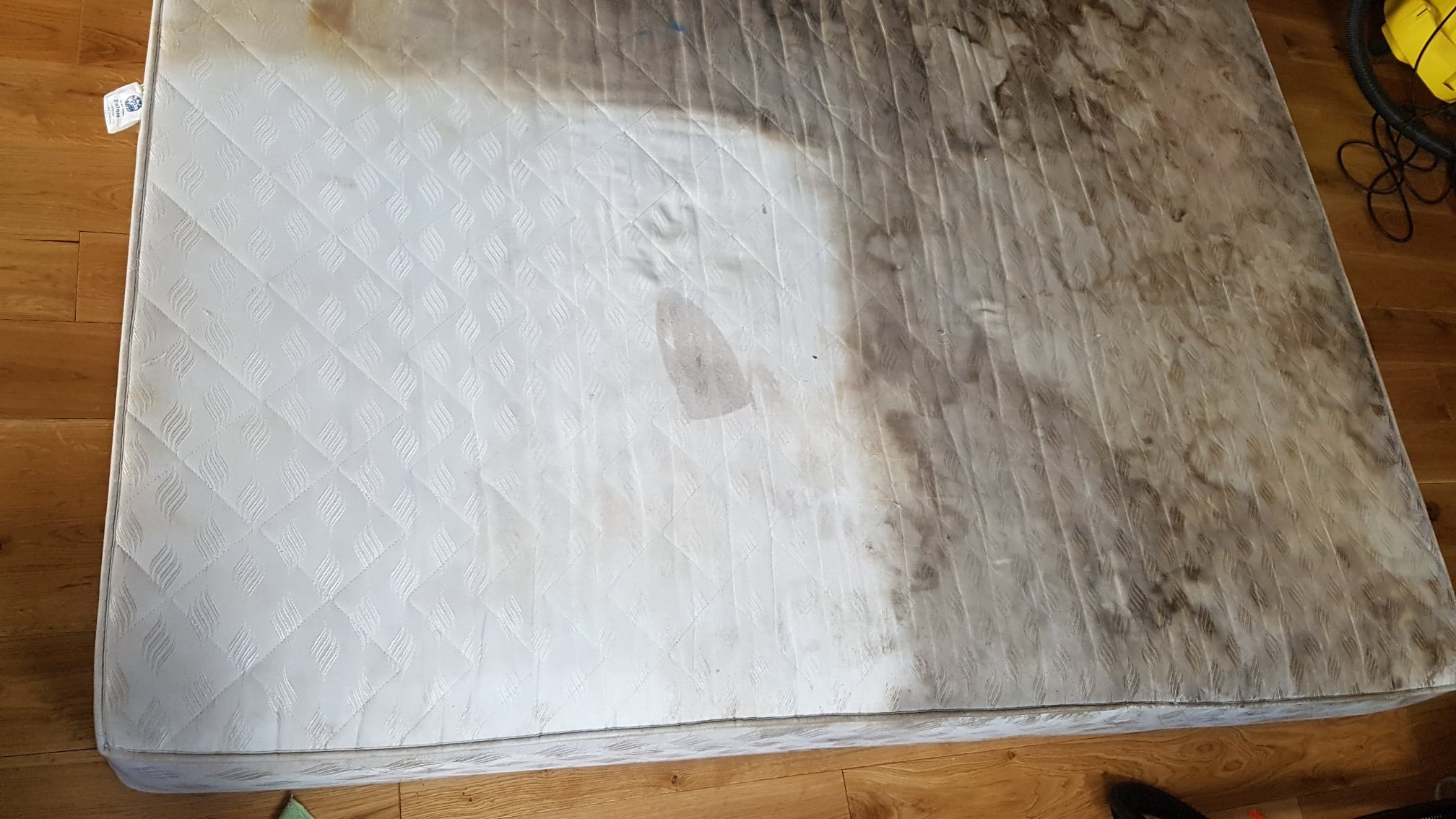 Częściowo wyczyszczony materac w Kielcach, widoczne wyraźne różnice w kolorze i stopniu zabrudzenia między obszarem po lewej stronie a prawą, silnie zabrudzoną częścią. Na powierzchni widoczny ślad...