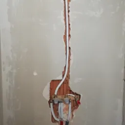 Ściana w trakcie prac instalacyjnych: widoczne rury doprowadzające wodę, częściowo schowane w wyżłobieniu w ścianie, z widocznymi śladami po kuciu i niedokładnym tynkowaniu.