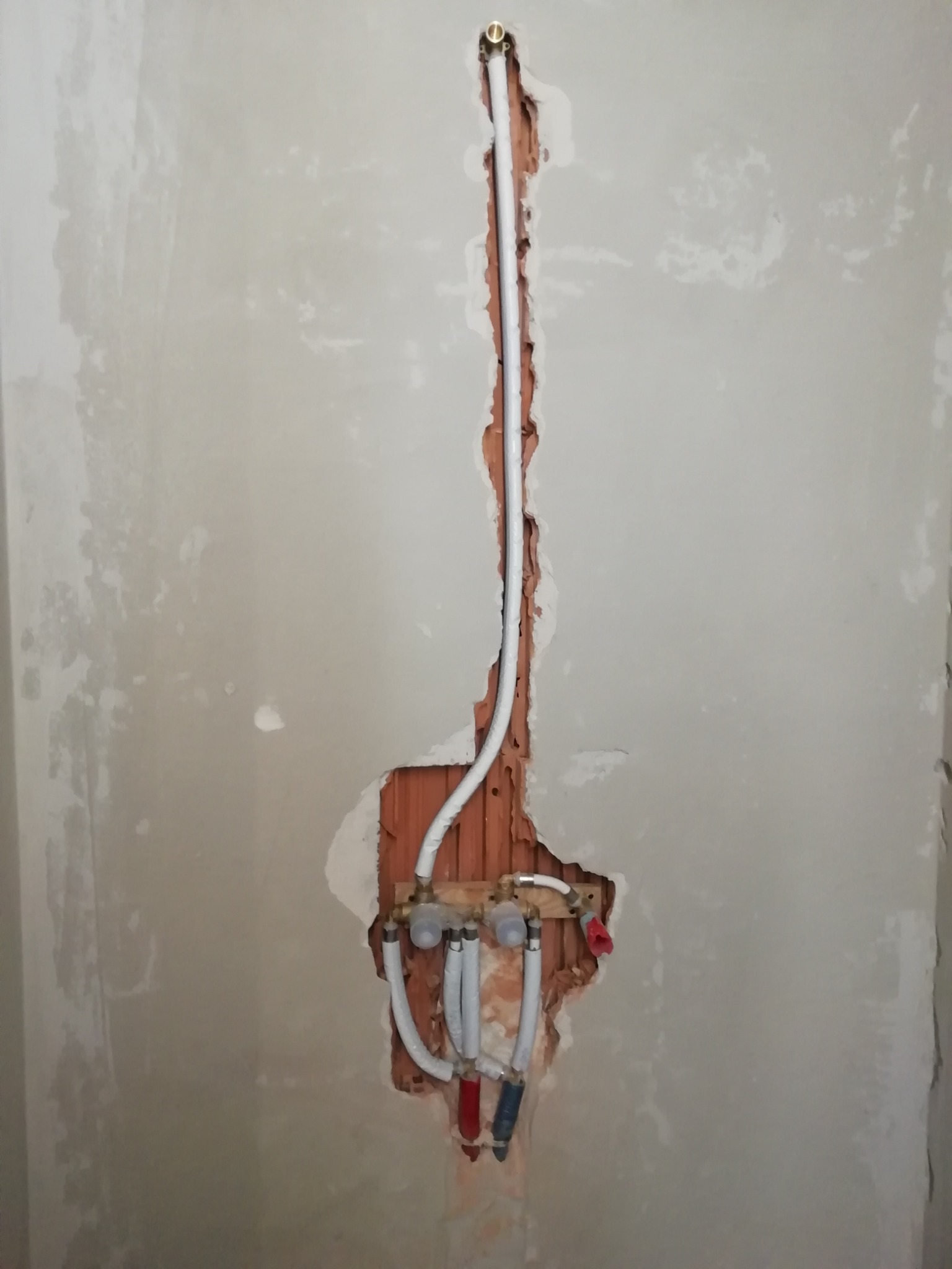 Ściana w trakcie prac instalacyjnych: widoczne rury doprowadzające wodę, częściowo schowane w wyżłobieniu w ścianie, z widocznymi śladami po kuciu i niedokładnym tynkowaniu.