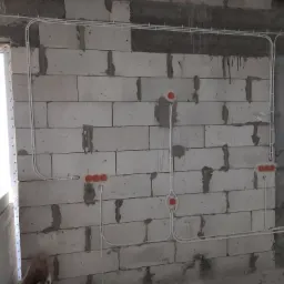 Białe kable elektryczne prowadzone po surowej ścianie z betonu komórkowego, widoczne puszki instalacyjne w kolorze pomarańczowym, instalacja w trakcie wykonywania.