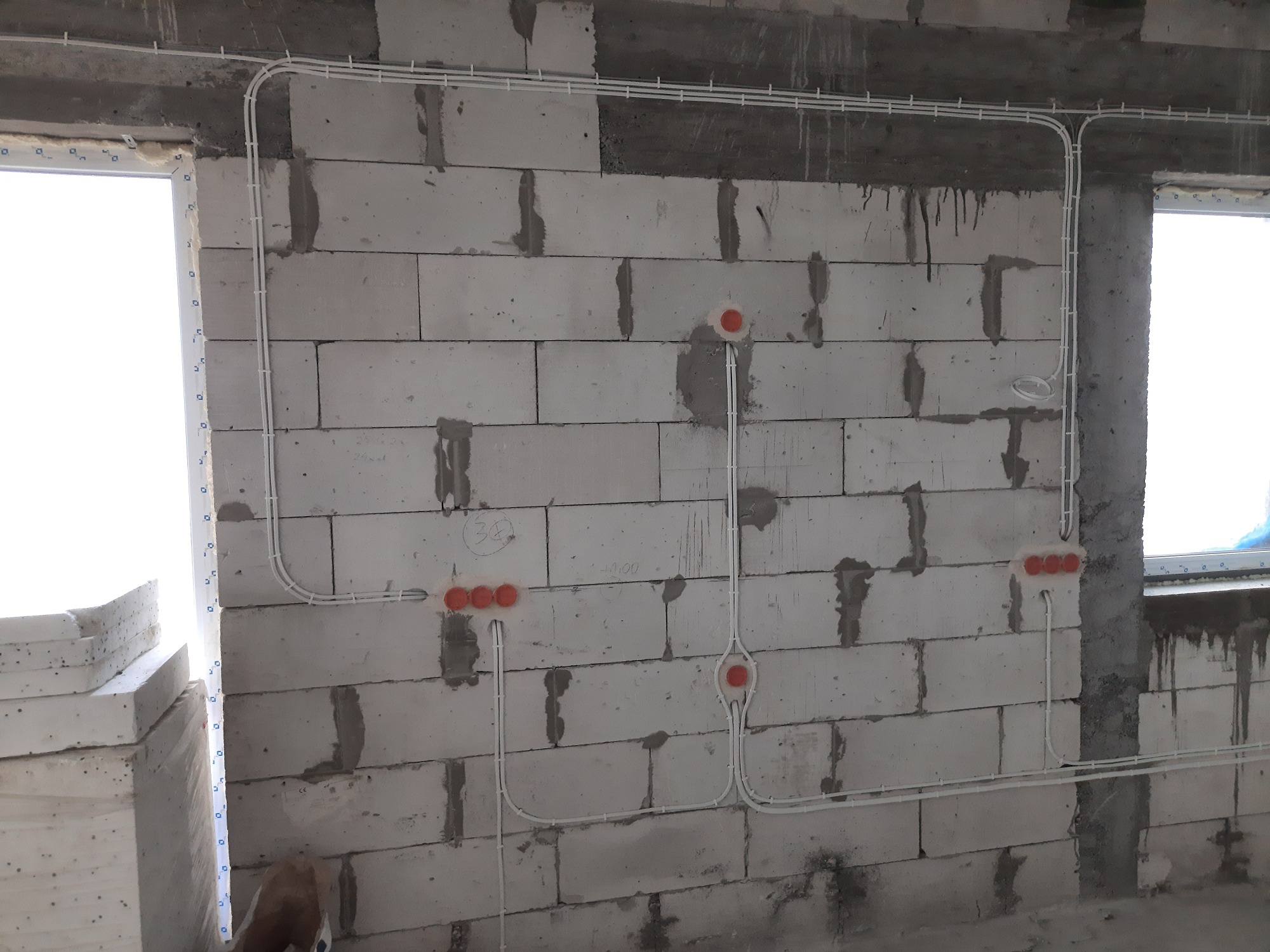 Białe kable elektryczne prowadzone po surowej ścianie z betonu komórkowego, widoczne puszki instalacyjne w kolorze pomarańczowym, instalacja w trakcie wykonywania.