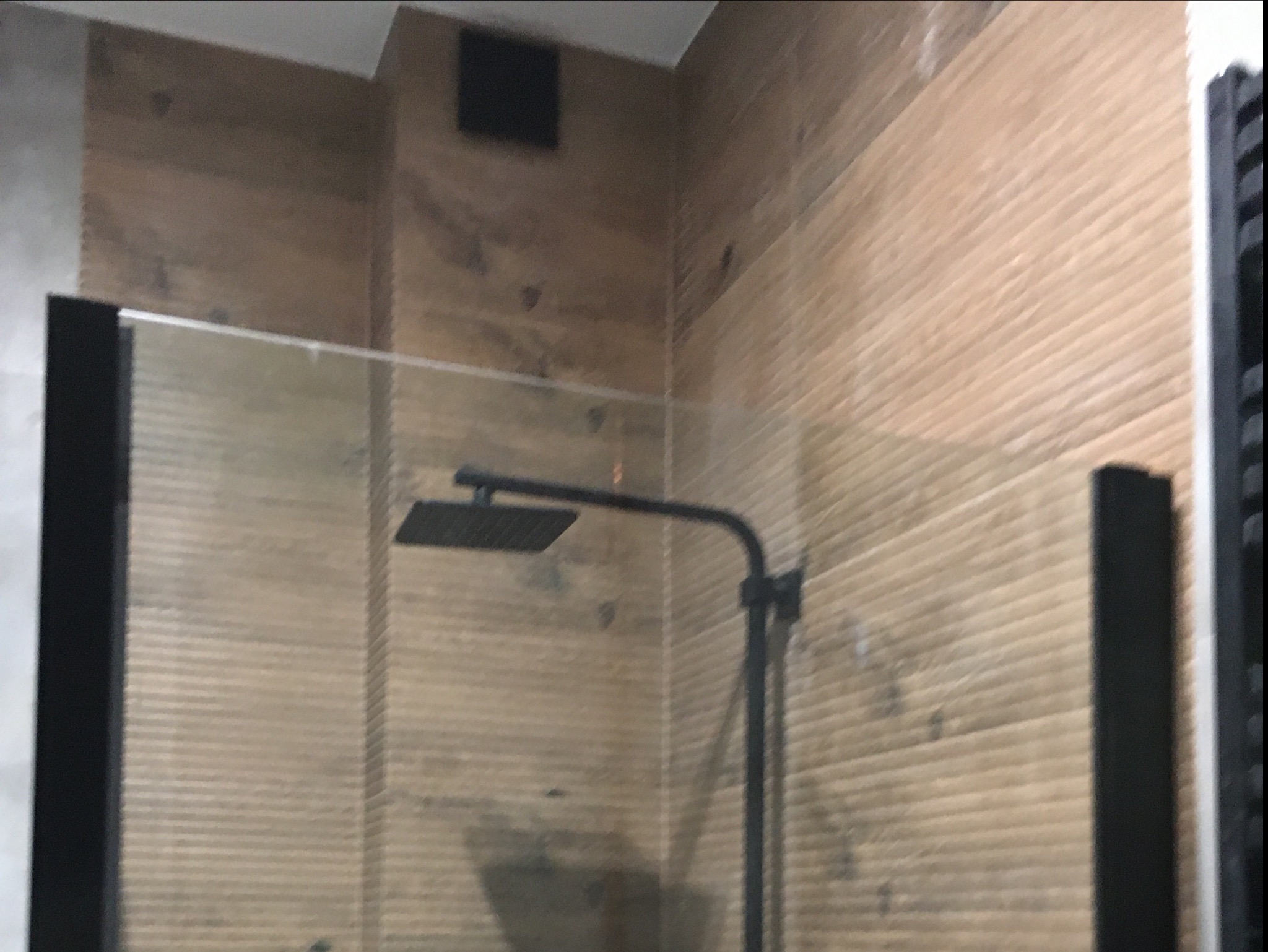 Nowoczesna kabina prysznicowa typu walk-in z czarną armaturą i ścianami wyłożonymi płytkami imitującymi drewno.