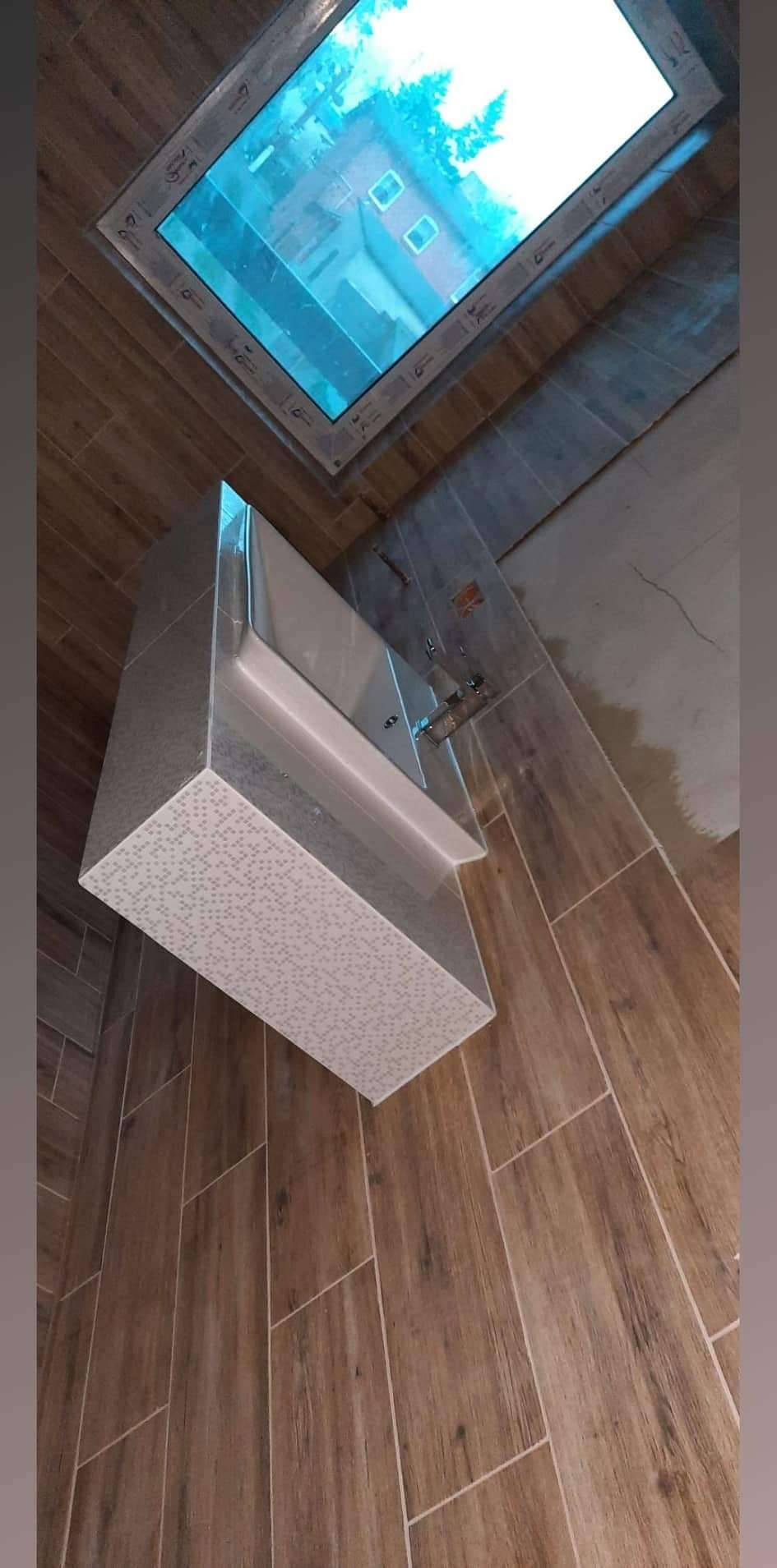 Nowoczesna umywalka z szafką wykończona płytkami z drobnym wzorem, zamontowana w łazience z drewnopodobnymi płytkami i oknem dachowym.