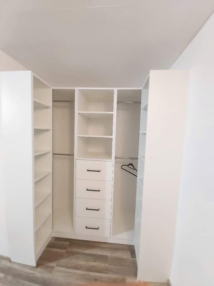 Biała, narożna garderoba z szufladami i półkami, widok od wewnątrz, pusta, na podłodze panele imitujące drewno.