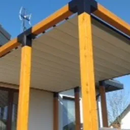 Konstrukcja z jasnego drewna i czarnych łączników tworząca zadaszenie nad tarasem, widok od dołu, jasne niebo w tle.