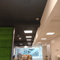 Wnętrze sklepu meblowego z widoczną kamerą monitoringu na czarnym suficie kasetonowym w pobliżu białej ściany.