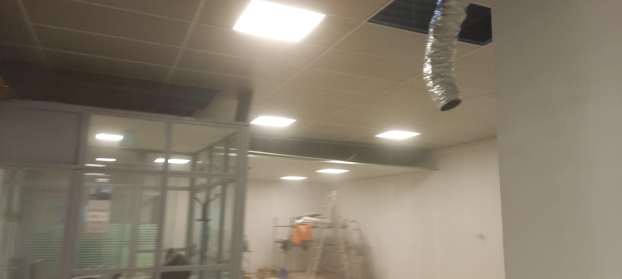 Montaż sufitu podwieszanego z widoczną instalacją wentylacyjną i elementami konstrukcyjnymi ścian działowych w przestrzeni biurowej.