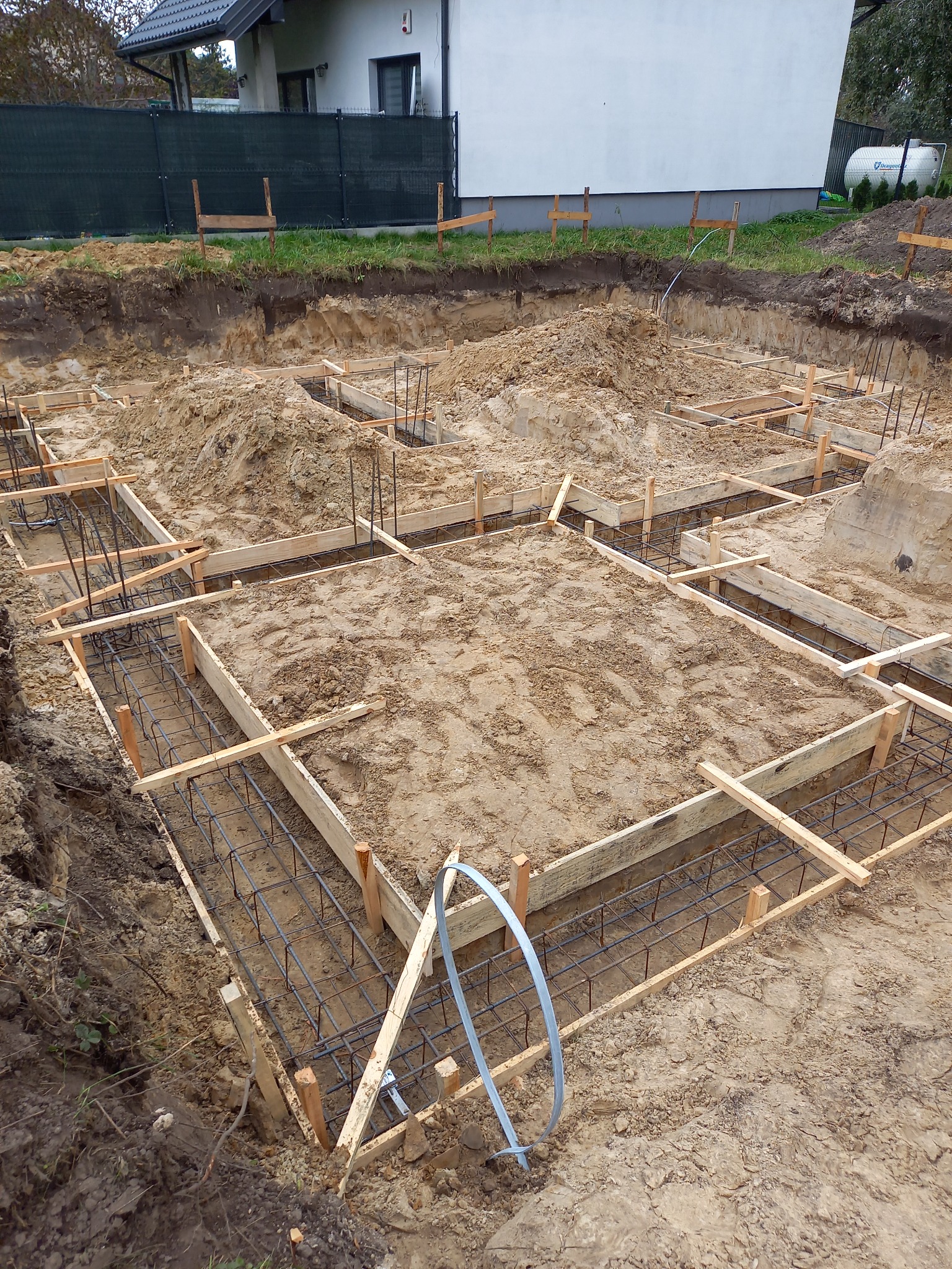 Przygotowanie fundamentów pod budowę domu: wykopane rowy z drewnianym szalunkiem i zbrojeniem stalowym, widok z góry na plac budowy w słoneczny dzień.