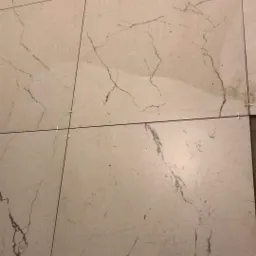 Ułożone płytki podłogowe imitujące marmur z krzyżykami dystansowymi w spoinach, widoczne niedoskonałości podłoża.