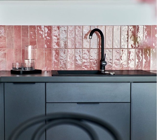 Wrocław: Nowoczesna kuchnia z szarymi szafkami i różowymi, błyszczącymi płytkami wertykalnymi nad blatem, uzupełniona czarną armaturą i szklanym dzbankiem.