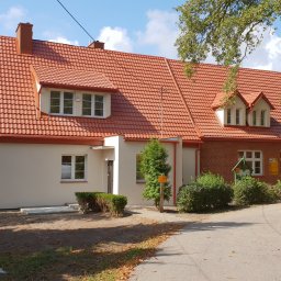 Firma Handlowa Dokument - Odnowiony budynek z czerwoną dachówką, kremową elewacją i ceglanym fragmentem, widoczny z poziomu ulicy w słoneczny dzień.