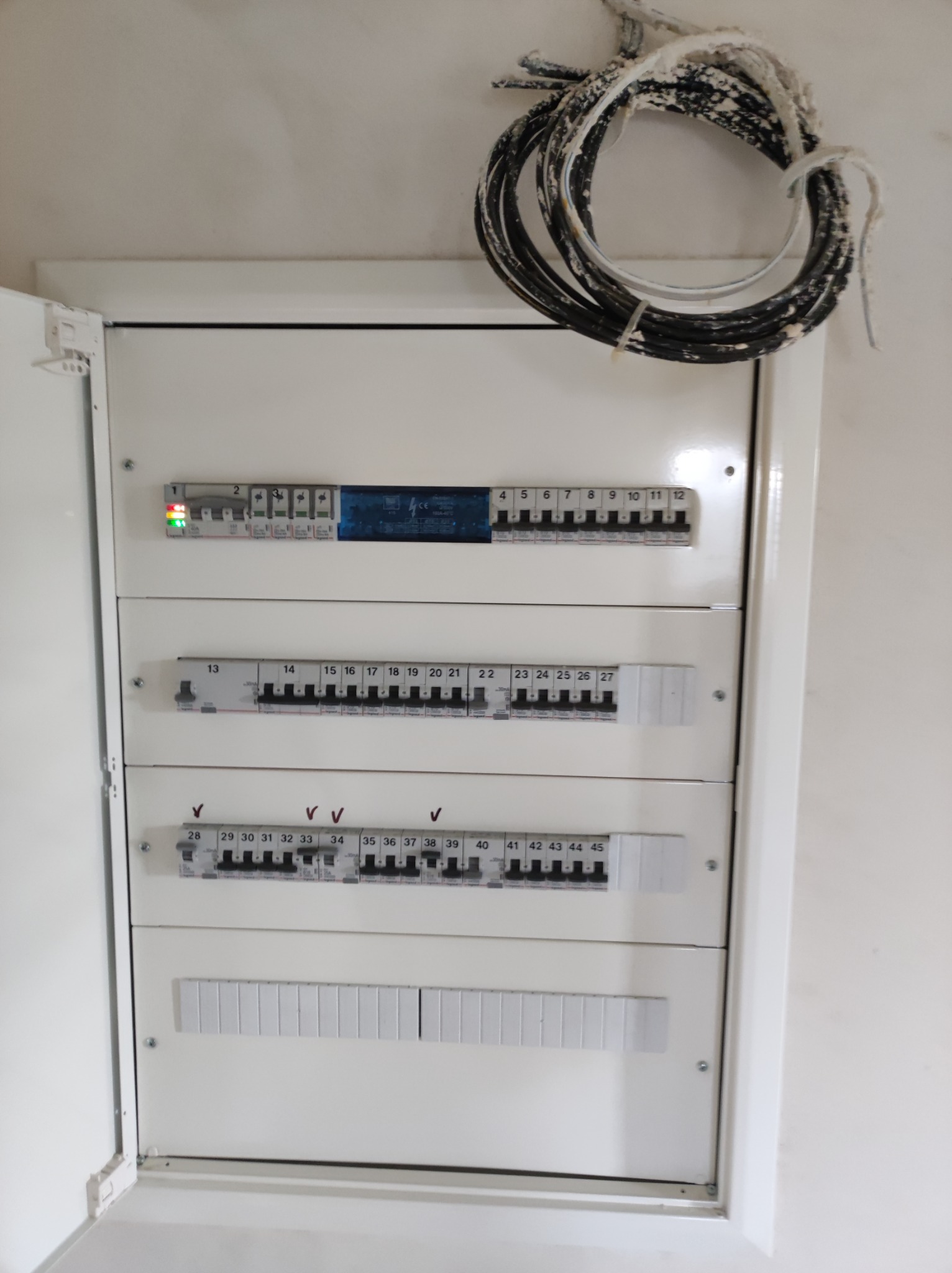 Rozdzielnica elektryczna z widocznymi bezpiecznikami i przewodami, część z nich przymocowana do ściany nad rozdzielnicą. Jeden z bezpieczników włączony, sygnalizowany zieloną diodą.