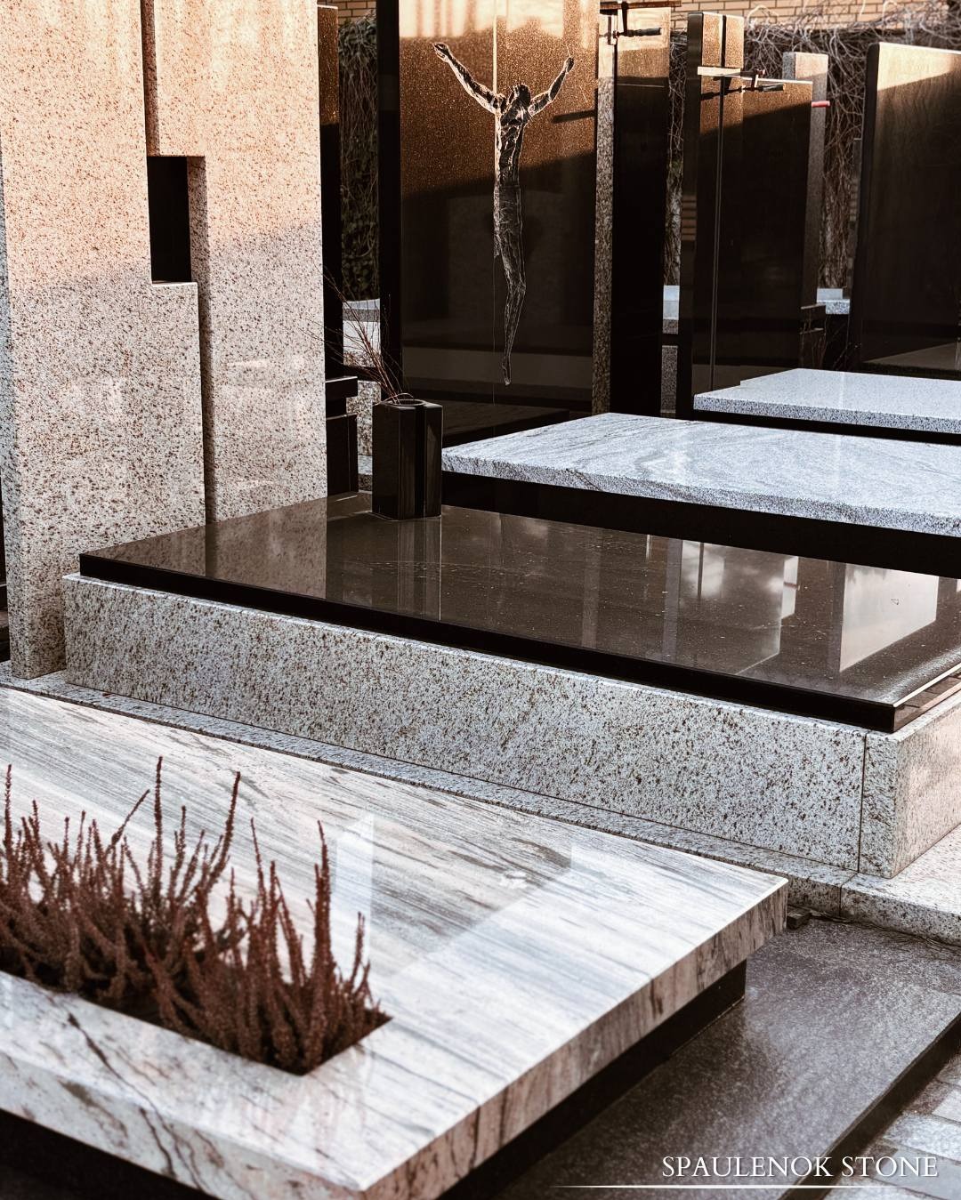 Granitowe nagrobki z rzeźbą Chrystusa i roślinami w donicach, prezentujące różne wzory kamienia i wykończenia.