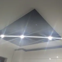 Nowoczesny sufit z wpuszczonym, ciemnym panelem i oświetleniem punktowym, widok z dołu w kierunku białych szafek kuchennych.