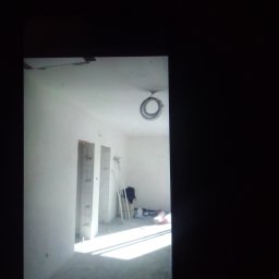 Anna Gębska - Wnętrze w trakcie prac wykończeniowych: białe ściany, przygotowane otwory drzwiowe, zwój kabli pod sufitem, rozproszone światło słoneczne.