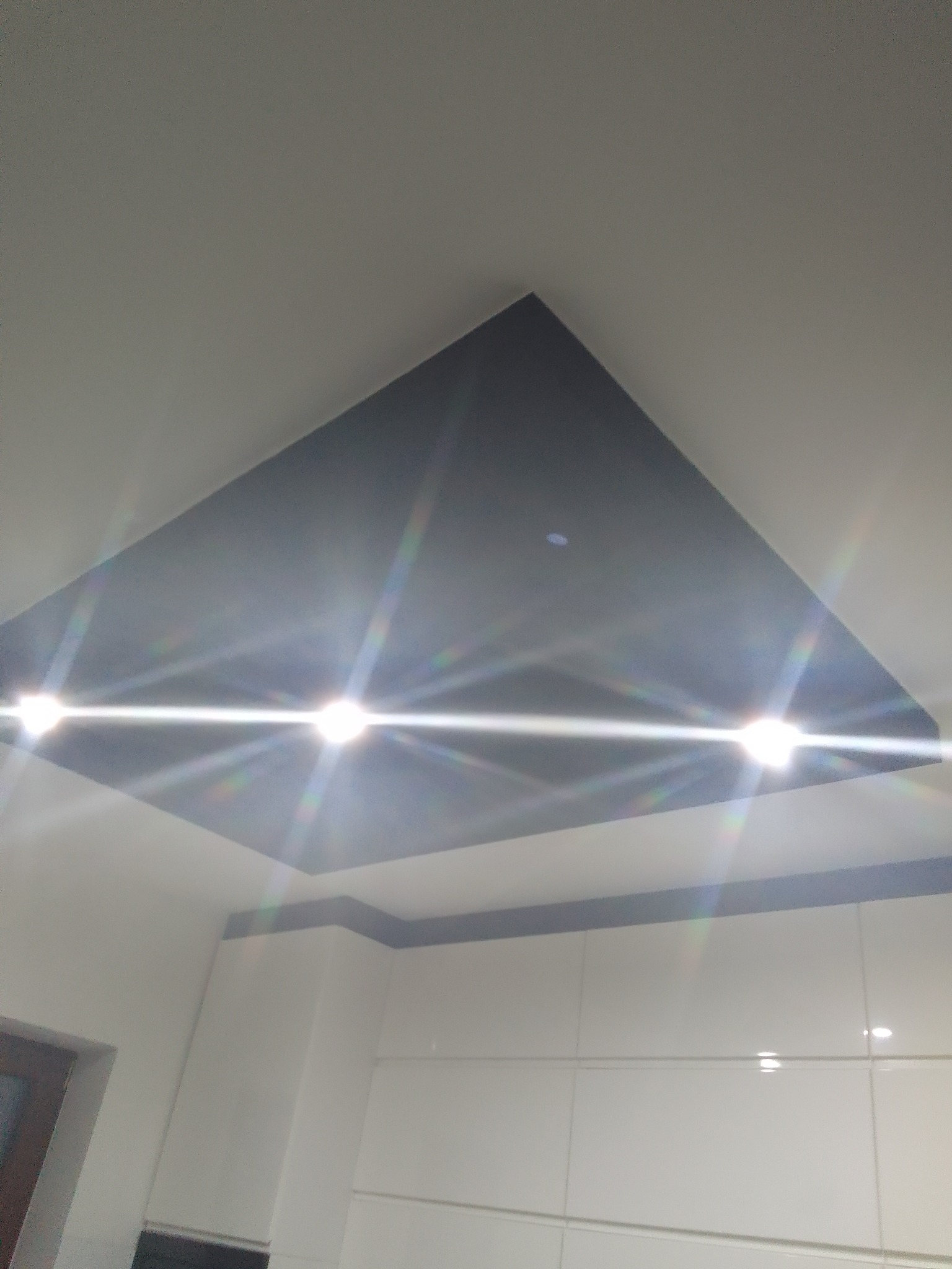 Nowoczesny sufit z wpuszczonym, ciemnym panelem i oświetleniem punktowym, widok z dołu w kierunku białych szafek kuchennych.