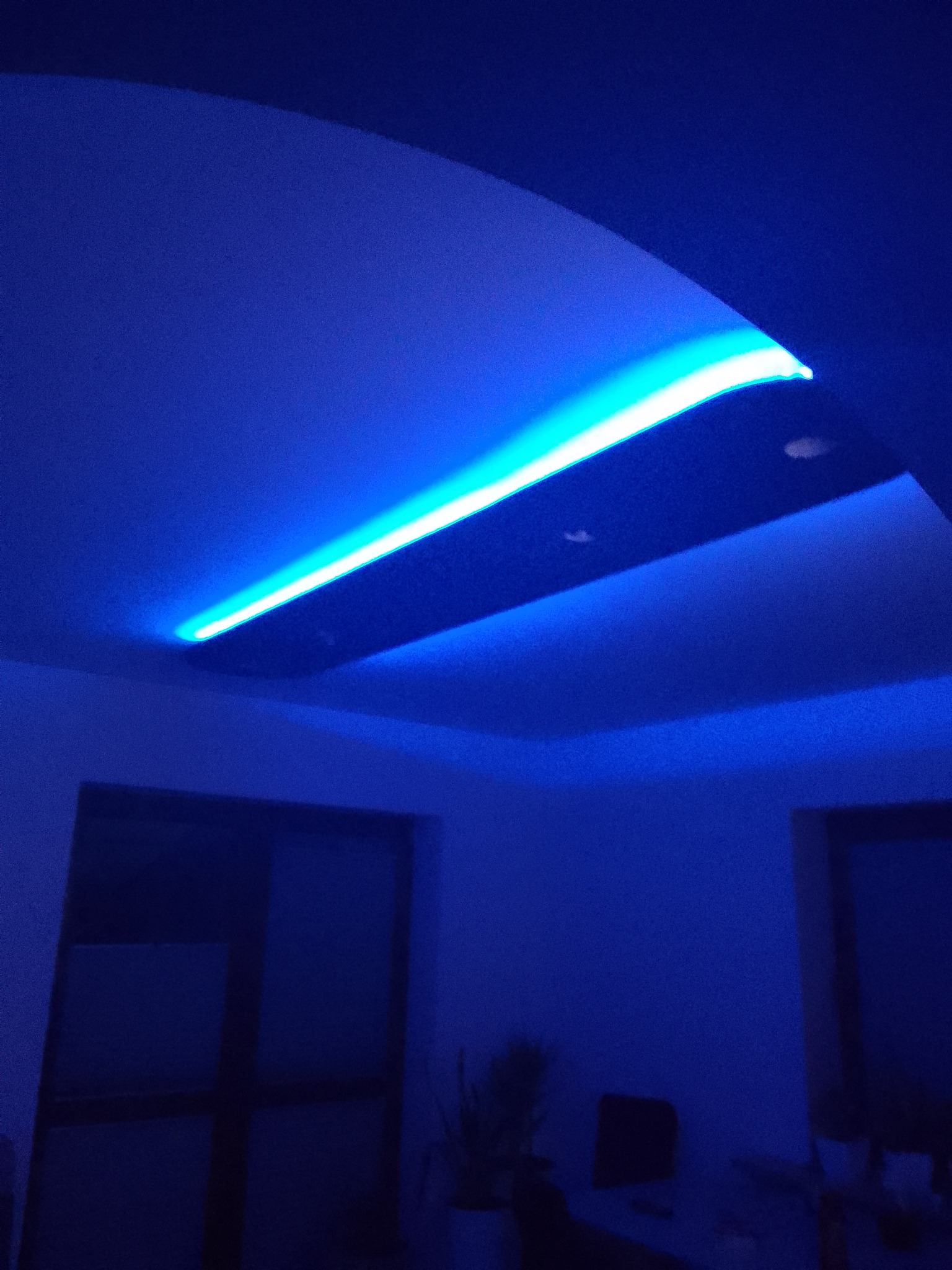 Niebieskie podświetlenie sufitu podwieszanego, widoczne okno w tle, zdjęcie w ciemnym pomieszczeniu.