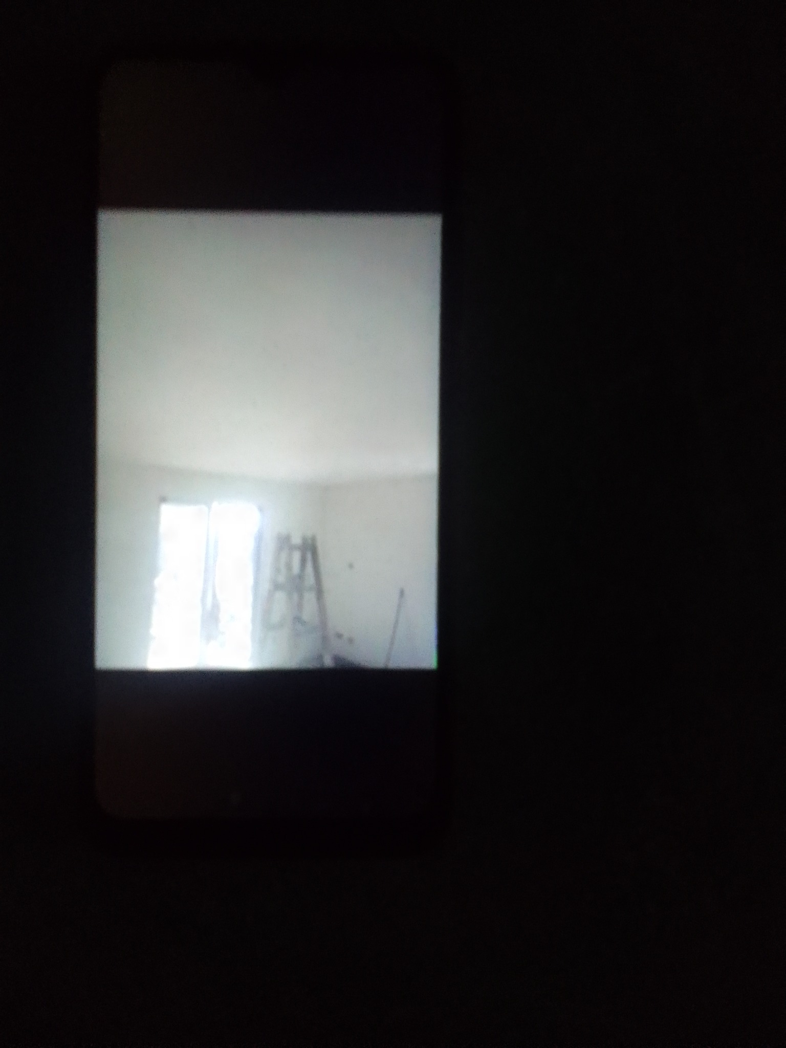 Zdjęcie pokoju w trakcie remontu, widoczna drabina, świeżo pomalowane ściany na biało, wykonane telefonem komórkowym w słabych warunkach oświetleniowych.