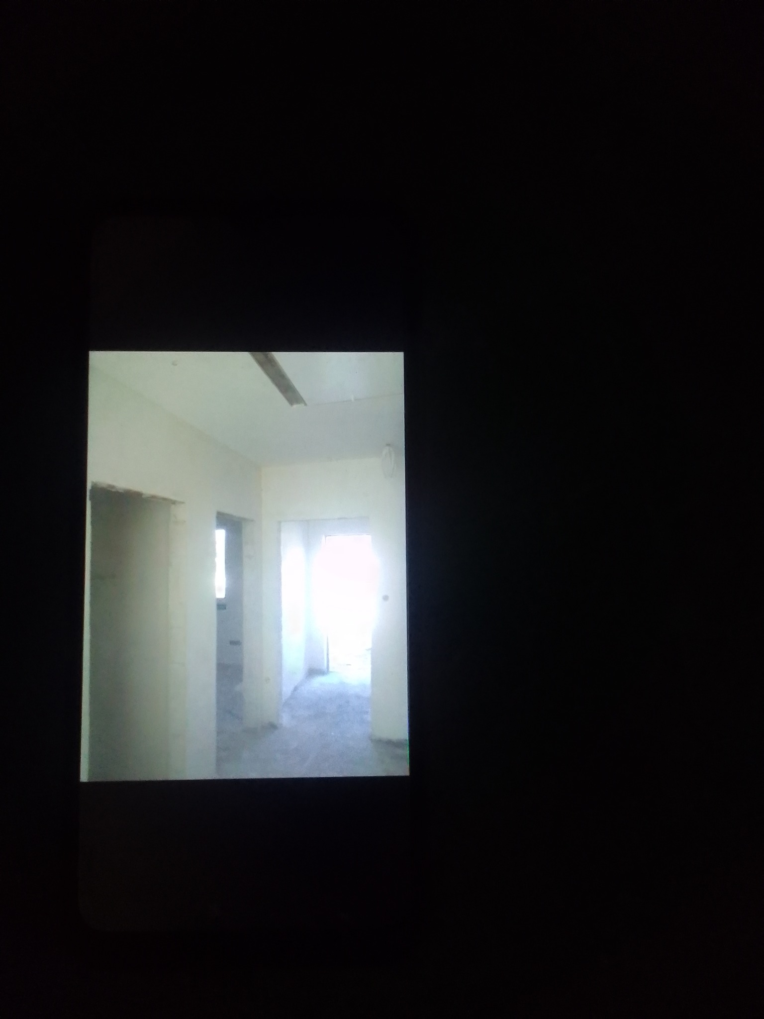 Wnętrze w trakcie remontu, widoczne surowe ściany, przygotowane otwory drzwiowe i okienne, oraz fragment drewnianej belki pod sufitem.