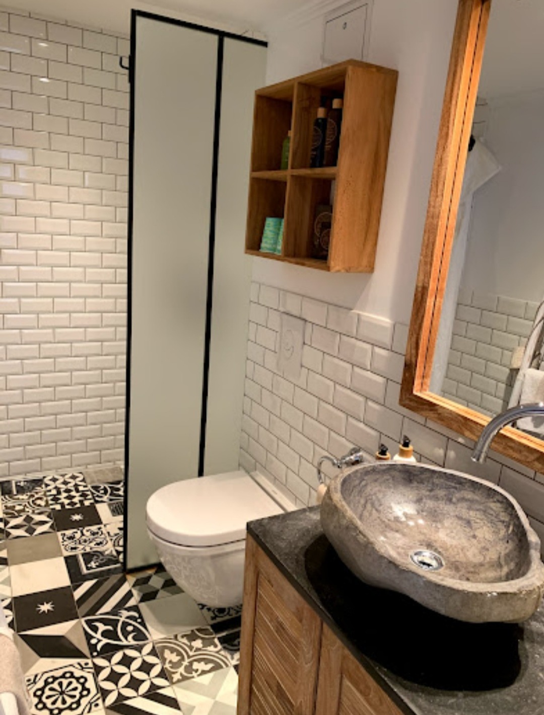 Wykończona łazienka z patchworkową podłogą, białymi kafelkami typu metro, kamienną umywalką nablatową i drewnianymi szafkami.
