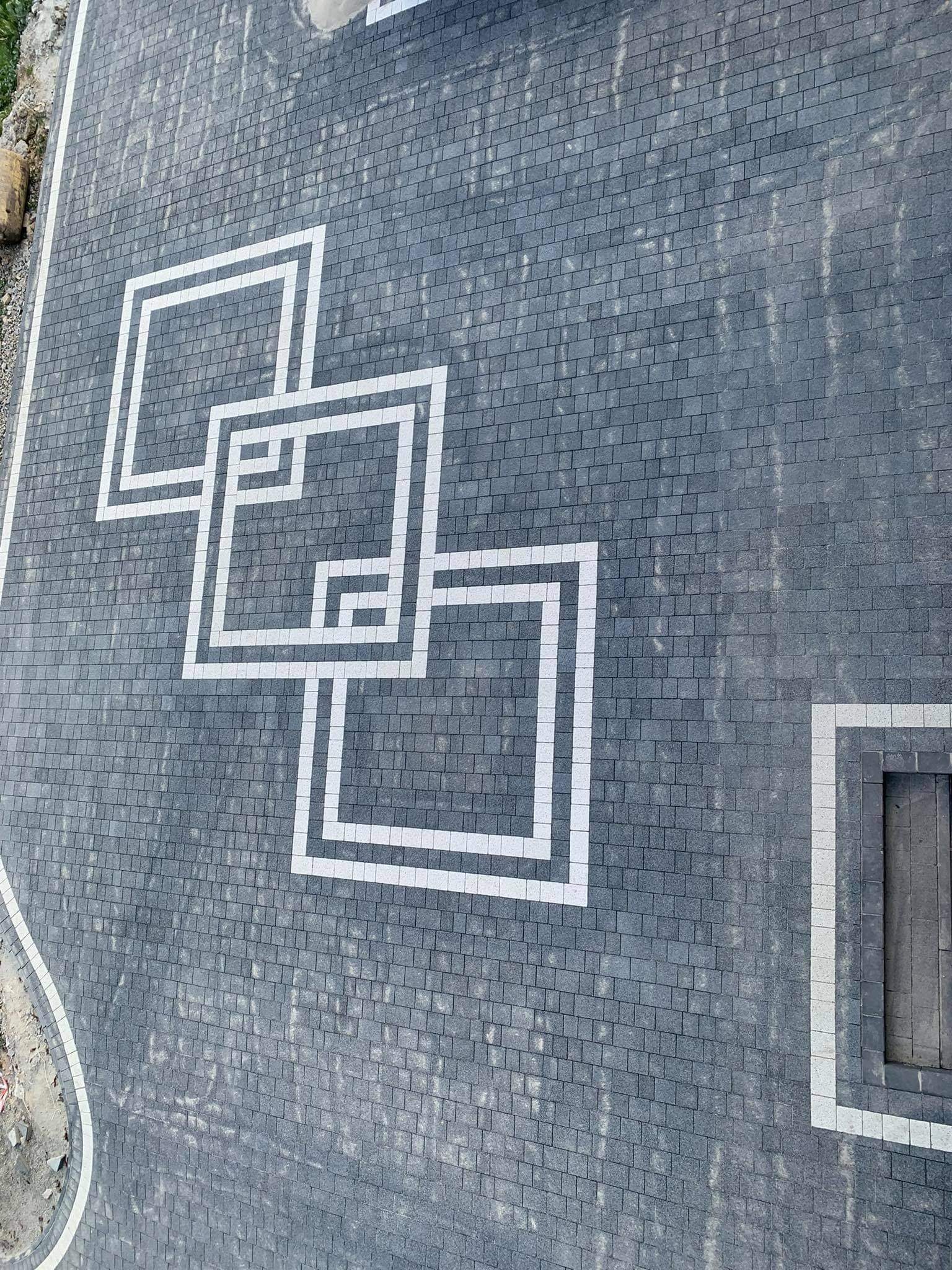 Widok z góry na szarą kostkę brukową z białym, geometrycznym wzorem z kwadratów, obok widoczne schody z kostki.