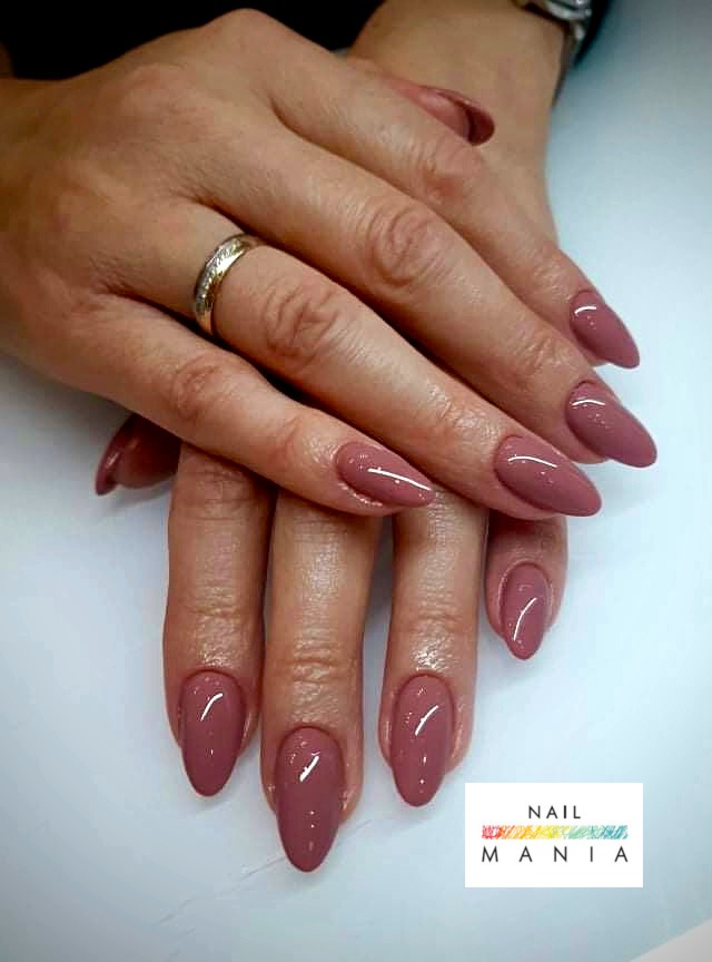 Dłonie z pomalowanymi na matowy, brudny róż paznokciami w kształcie migdała. Na palcu serdecznym złoty pierścionek z cyrkoniami. Widoczny fragment zegarka na nadgarstku.