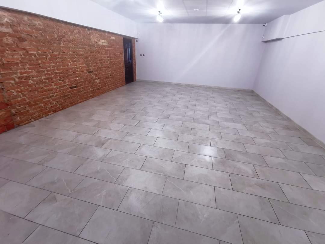 Wykończone wnętrze: szare płytki podłogowe ułożone w dużej, pustej przestrzeni z odsłoniętą czerwoną cegłą na jednej ścianie i pomalowanymi na biało pozostałymi ścianami.