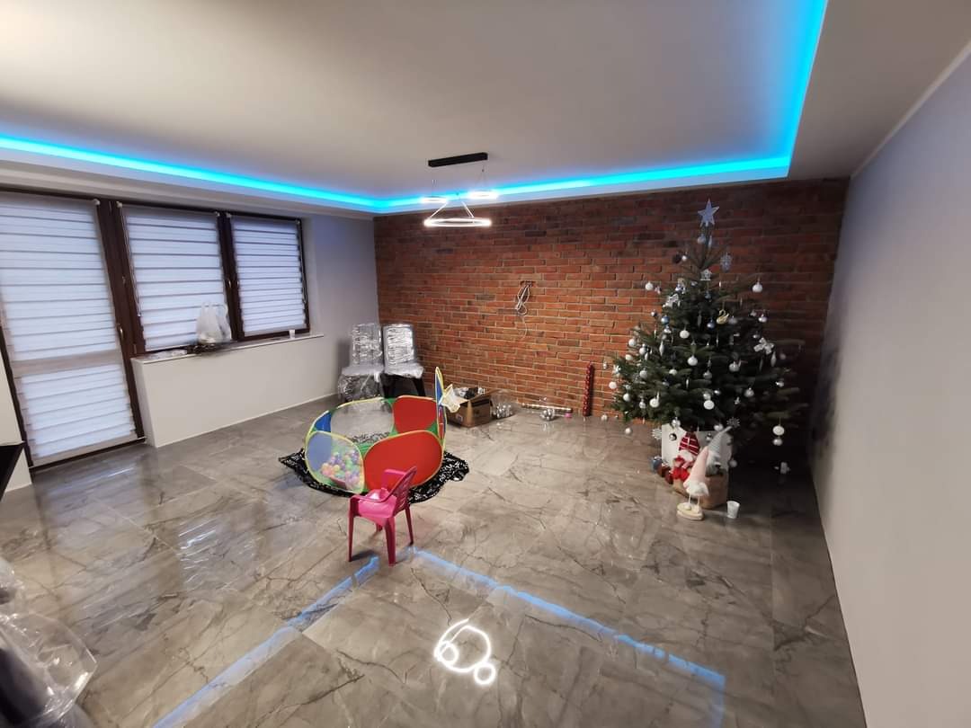 Pokój po remoncie z ceglaną ścianą, marmurową podłogą, podświetleniem sufitowym LED, choinką i zabawkami dziecięcymi, częściowo jeszcze w trakcie urządzania.