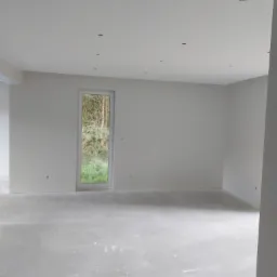 Wnętrze w stanie deweloperskim w Białogardzie, z wygładzonymi ścianami, przygotowane do dalszych prac wykończeniowych, widoczne otwory na oświetlenie w suficie i okno z widokiem na zieleń.