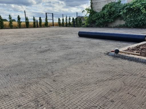 Przygotowany teren pod trawnik z siatką na krety, obrzeża z kostki, zwinięta czarna agrowłóknina i gumowy młotek na obrzeżu.