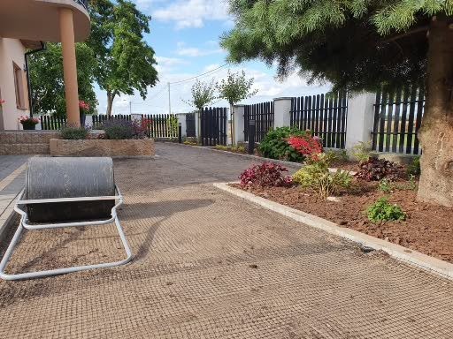 Przygotowanie terenu pod trawnik: wyrównana powierzchnia pokryta siatką na krety, widoczny walec ogrodowy, obrzeża rabat kwiatowych, czarne ogrodzenie panelowe w tle.