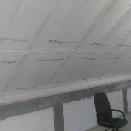 GOL MAR - Poddasze w trakcie ocieplania, widoczna biała membrana paroizolacyjna STEICO multi membra 5, ściany z białych bloczków, szara zaprawa, czarne krzesło biurowe w rogu.