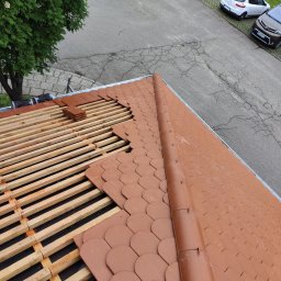 GOL MAR - Układanie brązowej dachówki karpiówki na łatach, widok z góry na fragment dachu i ulicę z zaparkowanymi autami. Częściowo ułożone dachówki.