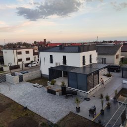 GOL MAR - Nowoczesny dom z płaskim dachem i pergolą, widok z góry. Szara kostka brukowa na podjeździe i wokół domu. Minimalistyczny design, jasna elewacja, ciemne akcenty.